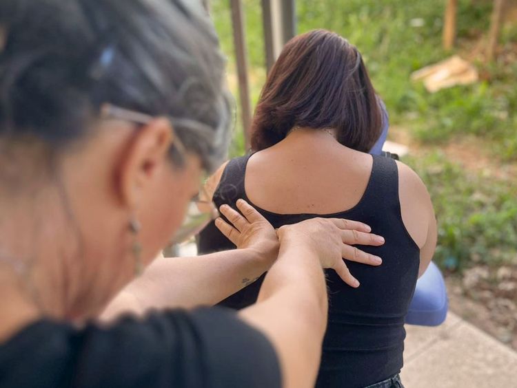 Photographie d'une personne de dos, assise sur une chaise de massage en extérieur. Nathalie masse et manipule le dos de cette personne.