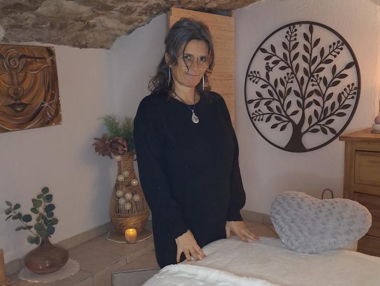 Photographie de Nathalie debout devant un lit de massage, regardant le photographe en souriant.