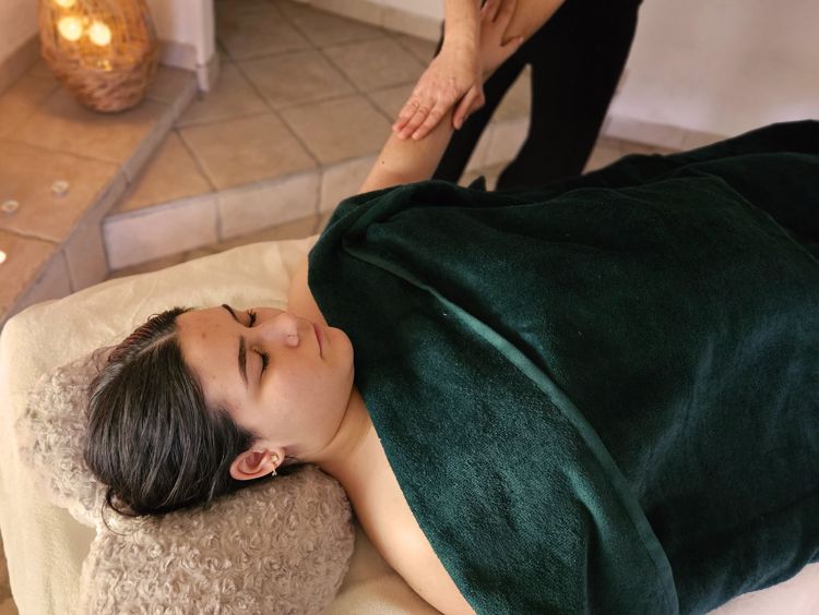 Photographie d'une femme allongée sur le dos sur une table de massage, le bras sorti pour être massé par Nathalie.