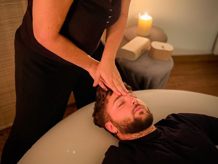 Photographie du buste d'un homme allongé sur un coussin d'air, se faisant masser le visage par Nathalie.