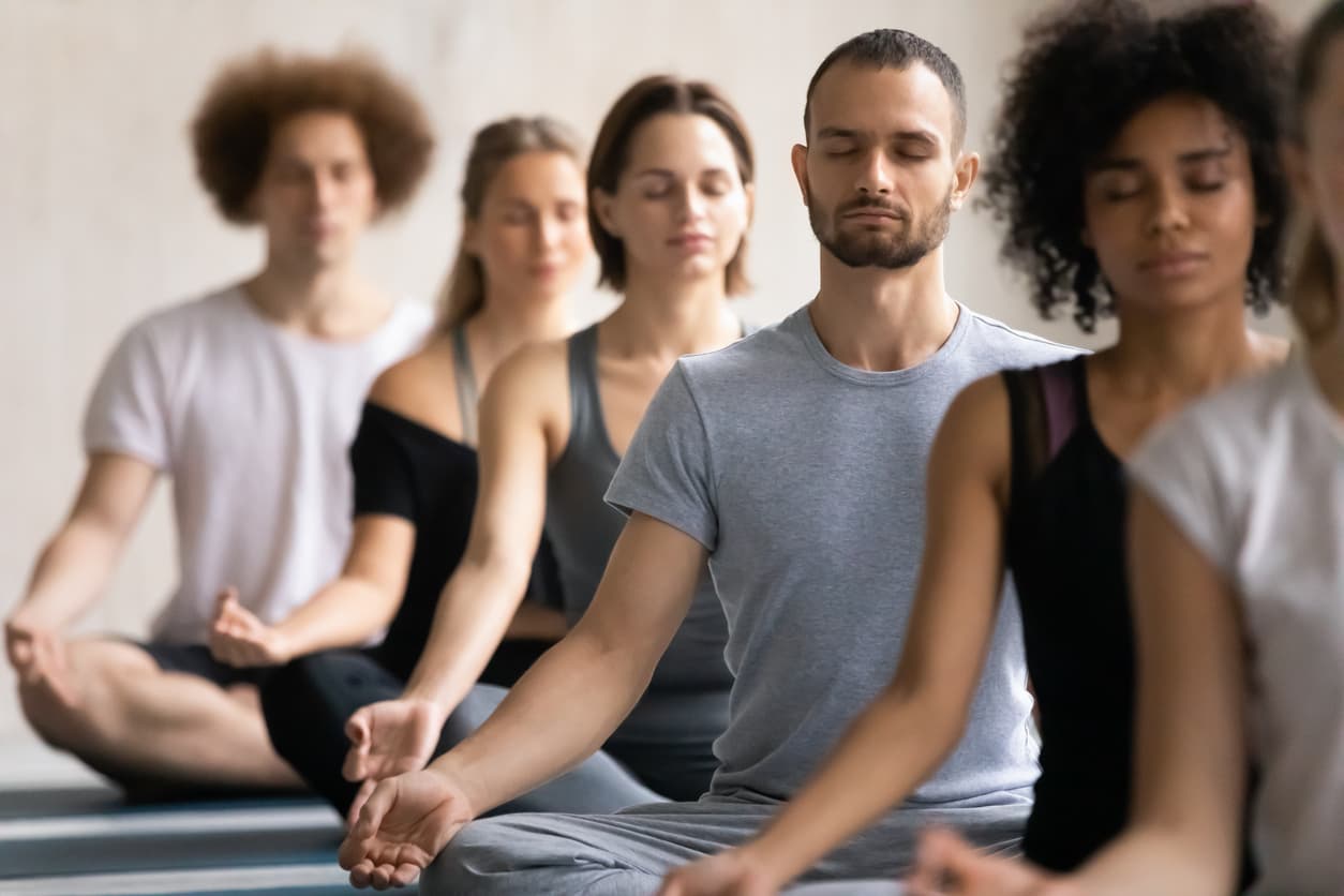 Photograhie d'un groupe de personnes en pleine méditation, assis les jambes en lotus.