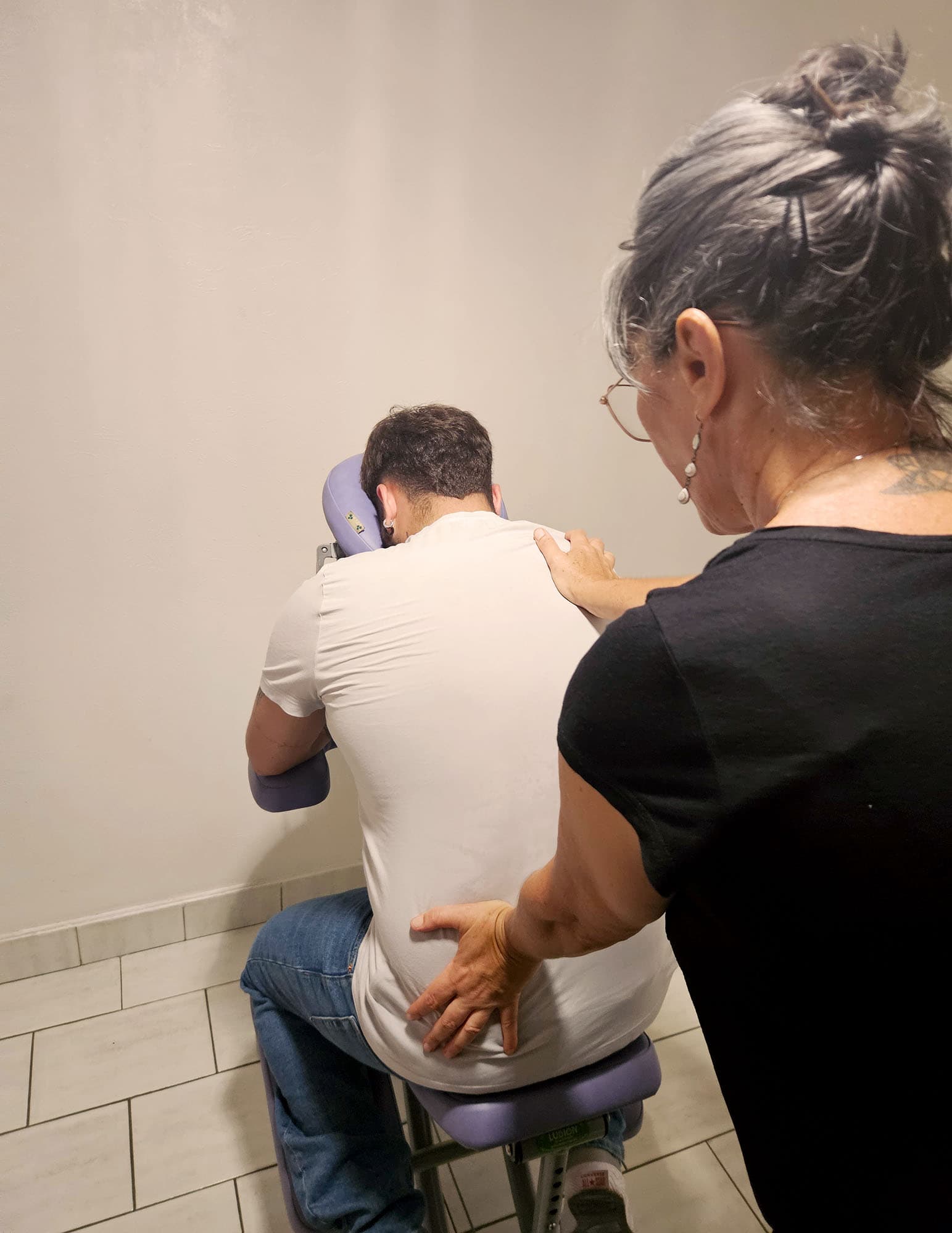 Photographie d'un homme assis sur une chaise de massage, de dos, se faisant manipuler le dos par Nathalie