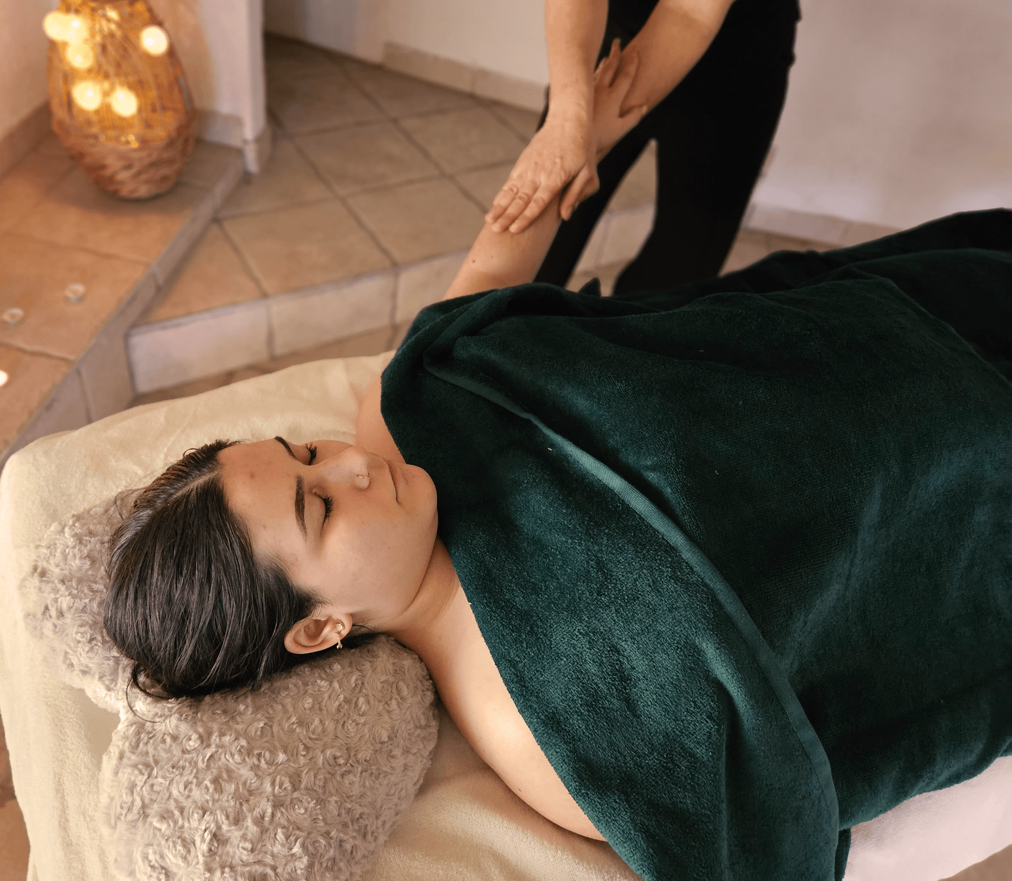 Photographie d'une femme allongée sur le dos sur une table de massage, le bras sorti pour être massé par Nathalie.